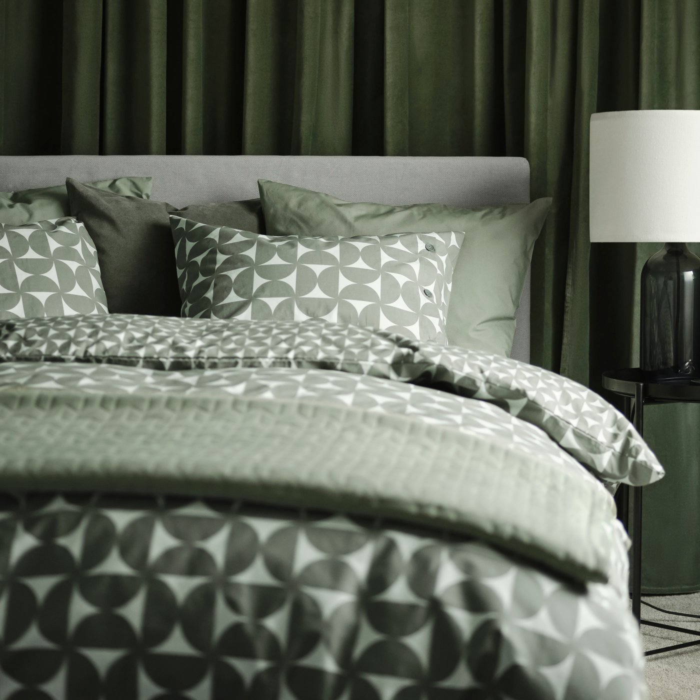 A Kabusa light grey GLADSTAD upholstered bed with four storage boxes dressed in grey/green ÄNGSNEJLIKA bed linen.