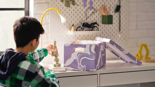 A patterned/lilac white TJENA storage box with lid in the childrens room