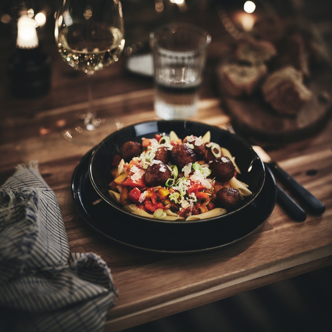 Ein Gericht aus Nudeln und Fleischbällchen in einer GLADELIG Schüssel auf einem Tisch, umgeben von einer Serviette, einem Wasserglas und einem Glas Sekt.