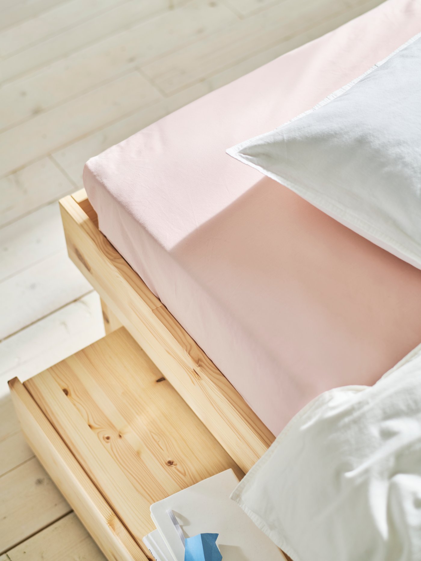 Close-up shot from above of GLAMBERGET bed frame with storage drawer and tray, pink DVALA fitted sheet on mattress.