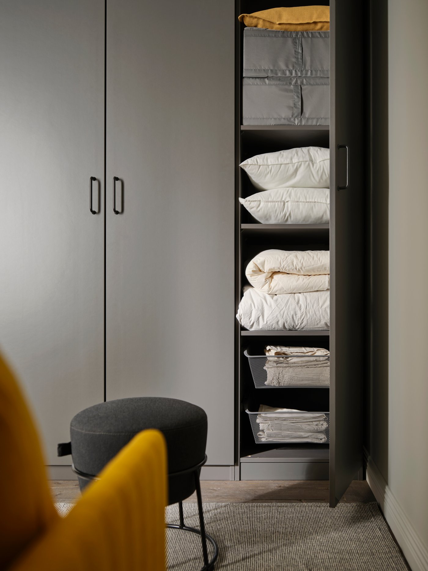 One dark grey FORSAND door is open on a PAX wardrobe. Inside are matching dark grey mesh baskets and clothes storage boxes.