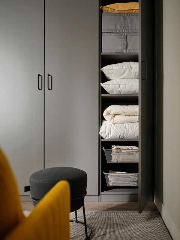 One dark grey FORSAND door is open on a PAX wardrobe. Inside are matching dark grey mesh baskets and clothes storage boxes.