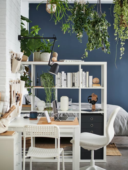 A white MELLTORP table with one white and one beige chair plus a black wall lamp above, beside a white KALLAX storage unit.