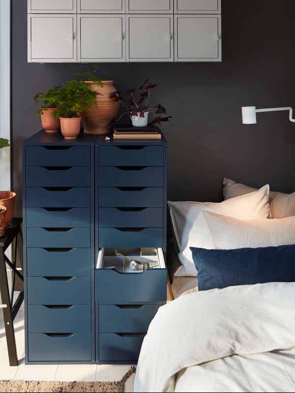 Zwei schmale, hohe Schränke mit vielen Schubladen stehen nebeneinander bei einem Bett. 
