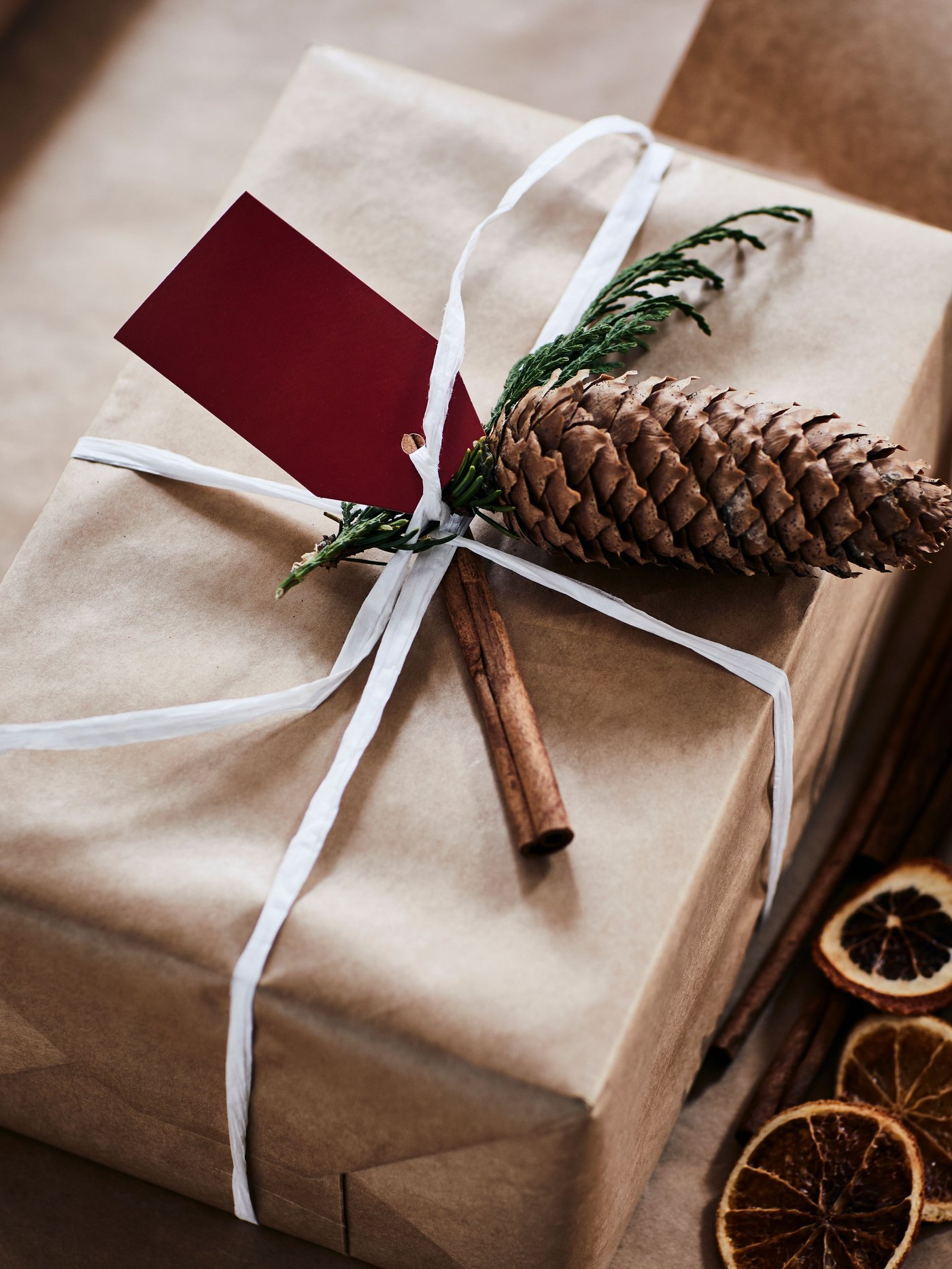 Julklapp men brunt papper och vitt snöre dekorerad ned en kotte.