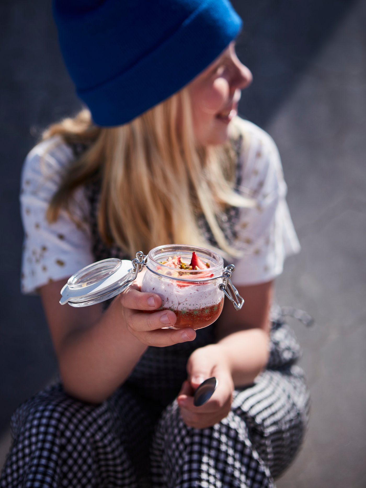 An opened KORKEN glass jar filled with a panna cotta-like dessert with toppings held by a young girl.