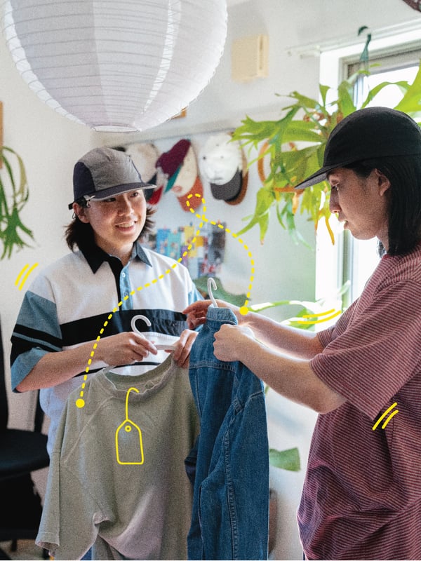 A person handing another person a hanger with a shirt on it.