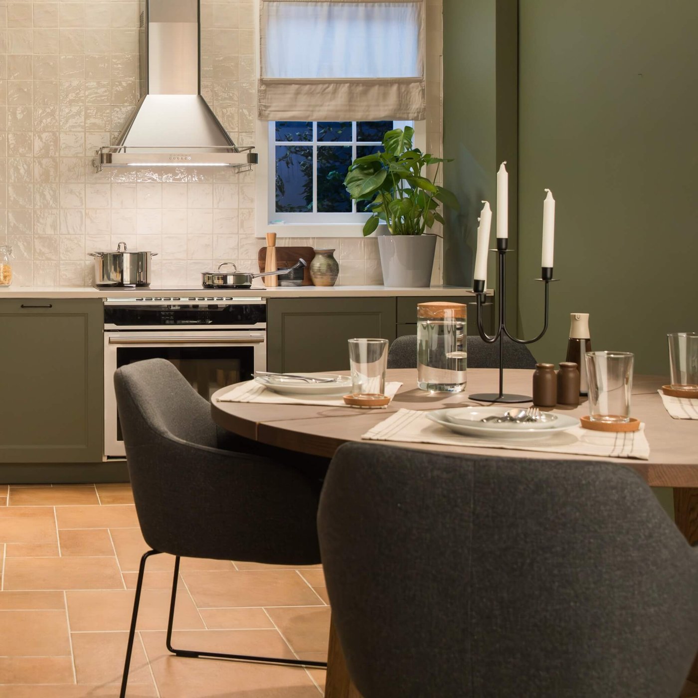 Cozy kitchen and dining area with AXSTAD green cabinets, set round table, warm terracotta tiles, and soft natural light.