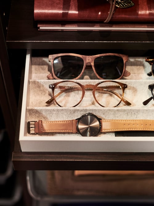 Un tiroir ouvert, montrant un rangement KOMPLEMENT gris avec différents types de lunettes et une montre.