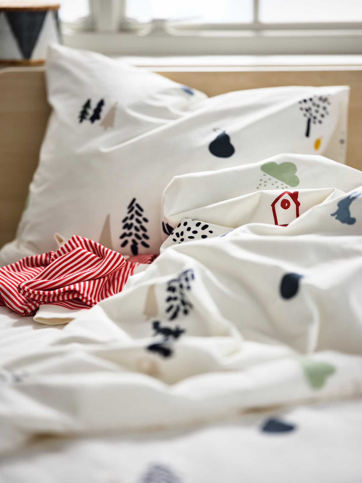 Tuala bayi dengan penutup kepala DRÖMSLOTT berwarna putih tergantung di antara kemeja-T pada penyangkut dengan mainan lembut pada rak dengan tombol kayu.