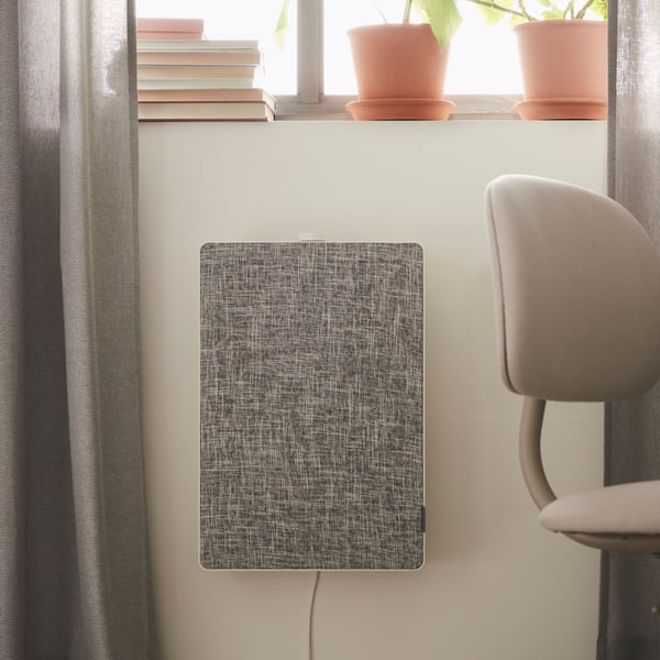 A FÖRNUFTIG air purifier is mounted on a wall underneath a window. There are some books and plants on the windowsill.