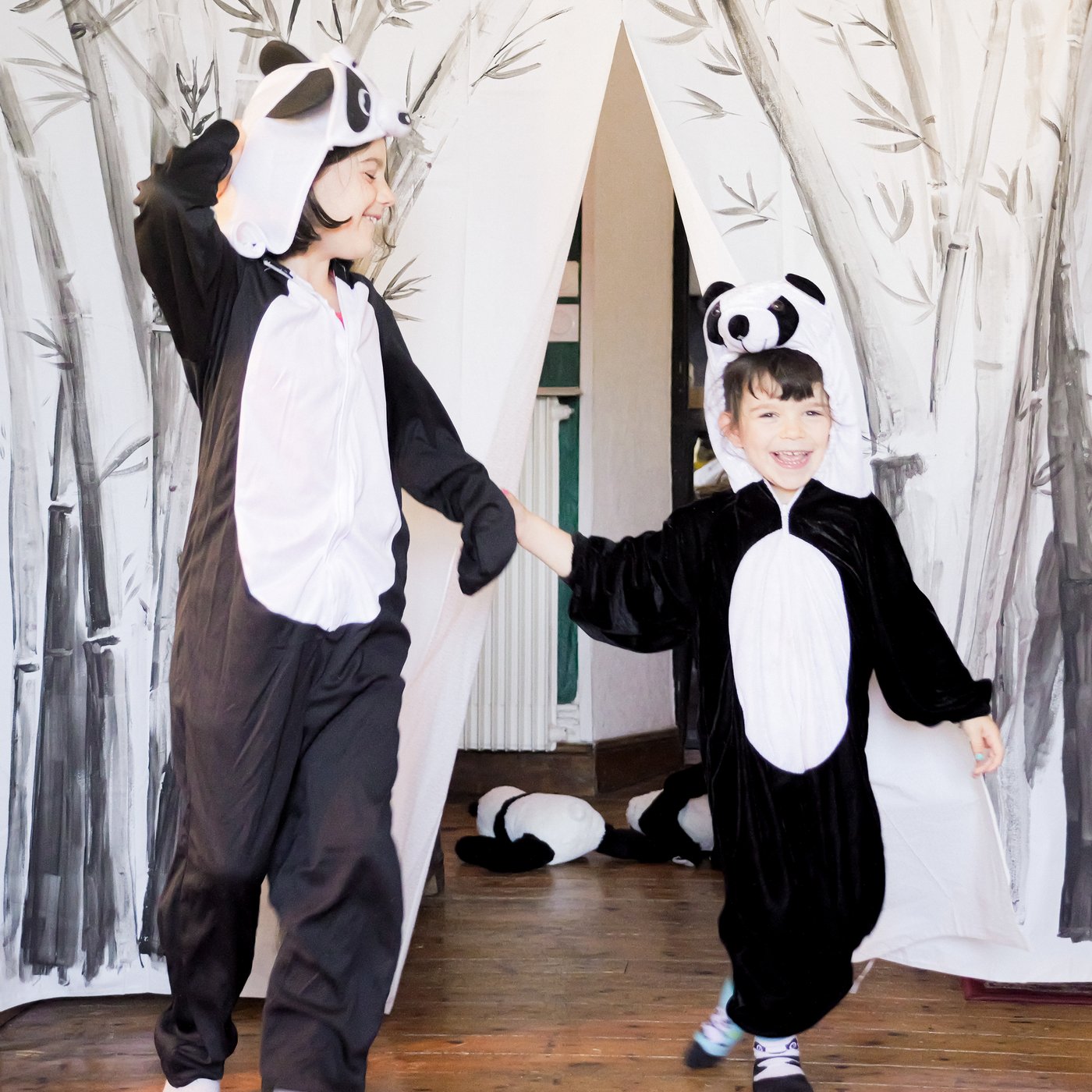 Two children in panda bear costumes take a bow in front of a stage curtain made from a decorated BJÄRSEN shower curtain.