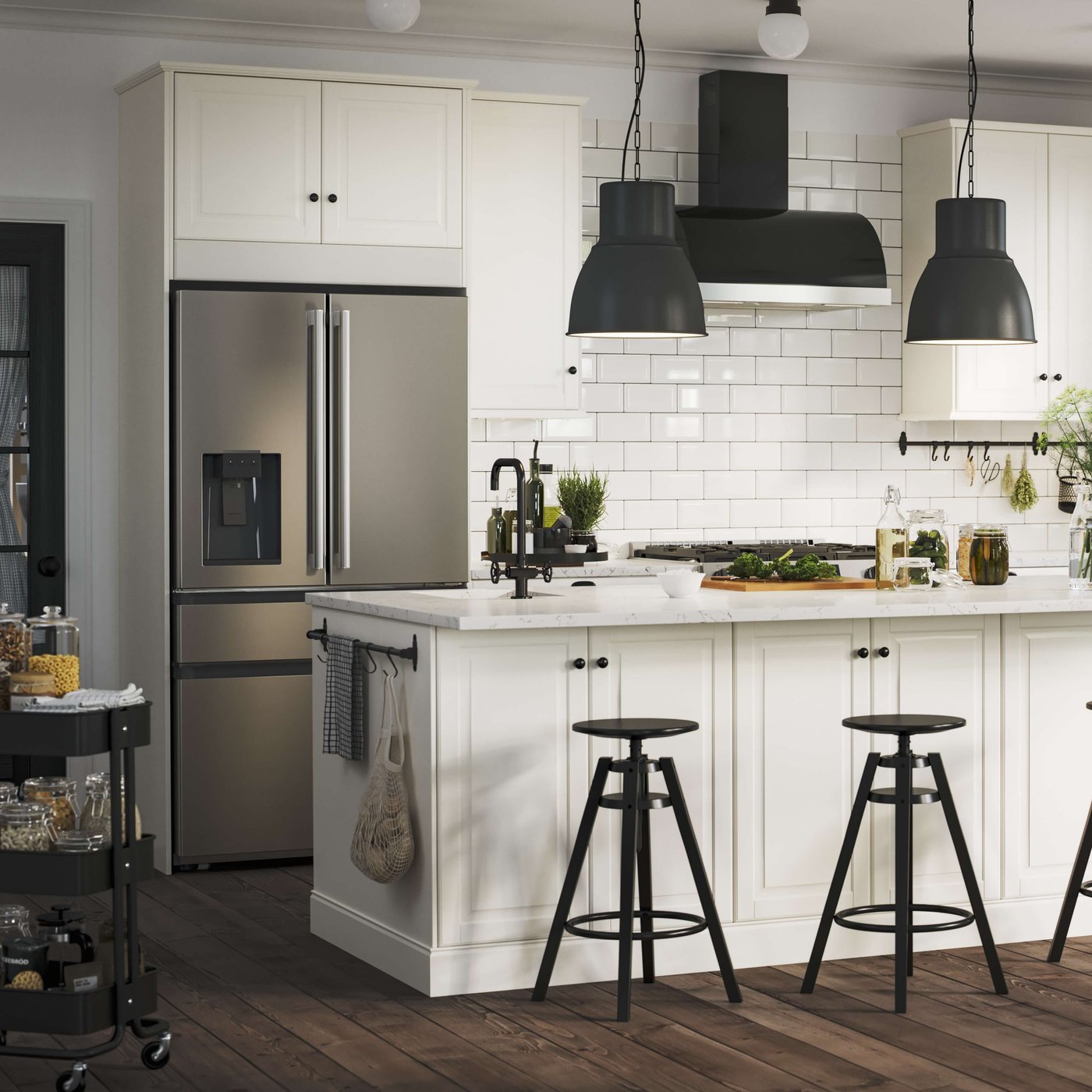 Modern white kitchen with island seating, stainless fridge, black pendant lights and tile backsplash.