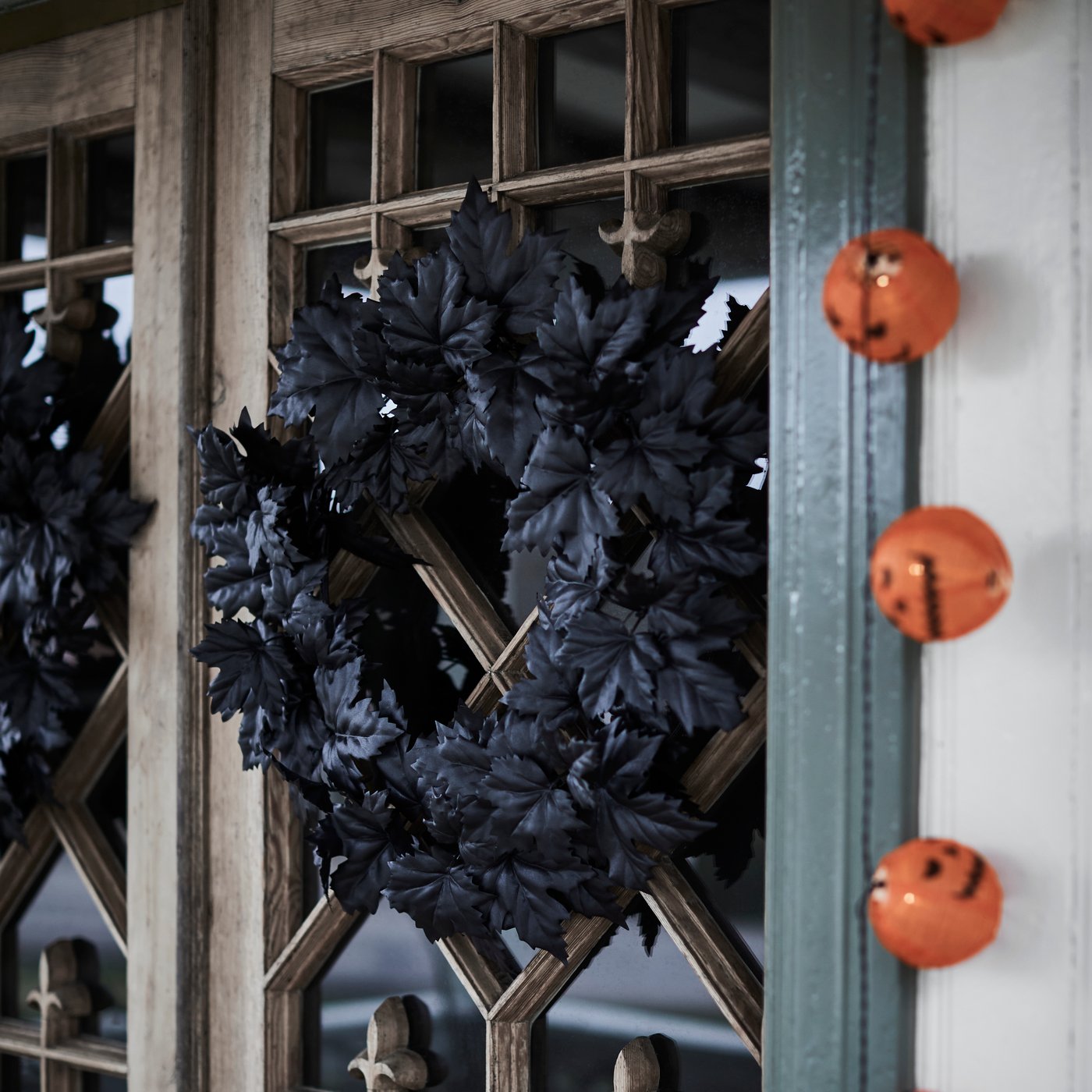 An angled shot of a front door with a black leafy wreath and pumpkin string lights hanging down.