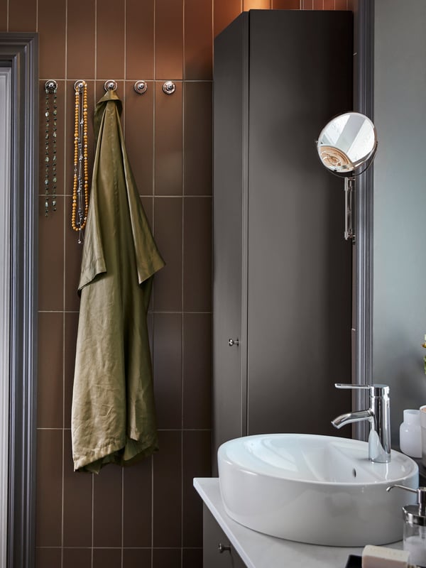 A wash-stand/wash-basin in dark-grey/white, a dark-grey high cabinet and five wall-mounted knobs in chrome effect.