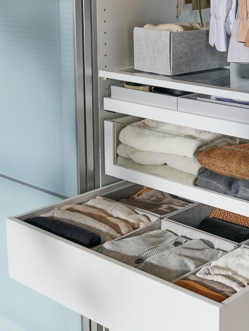 In einem Kleiderschrank ist eine geöffnete KOMPLEMENT Schublade in Weiß zu sehen, in der sich hellgraue KOMPLEMENT Boxen mit Accessoires befinden.