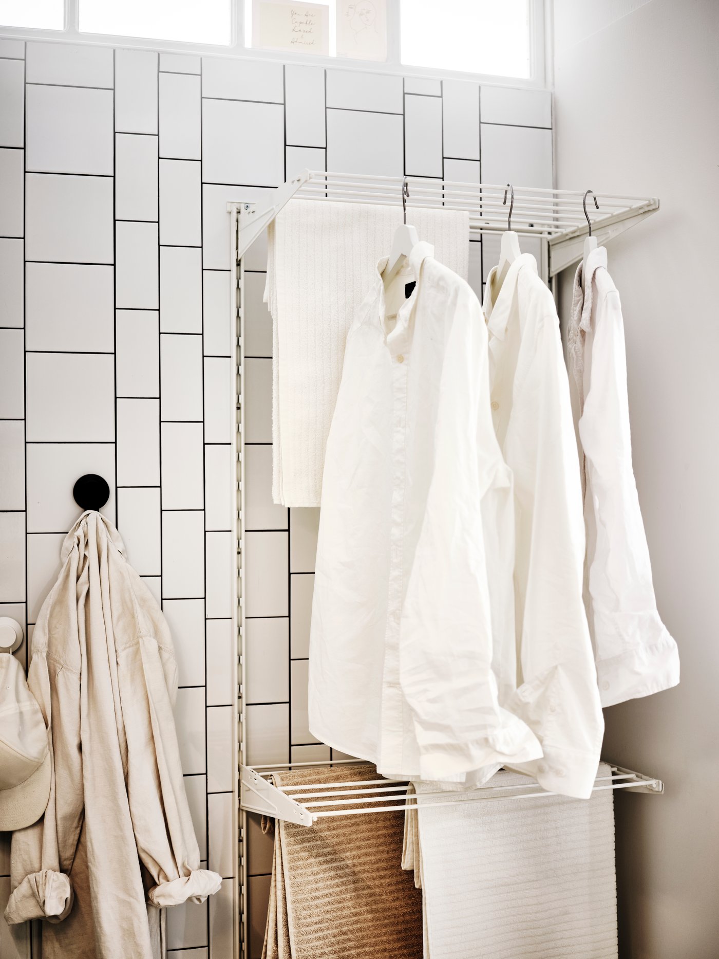 A bathroom with clothes and VÅGSJÖN bath towels hanging and drying on a white/metal BOAXEL laundry combination.