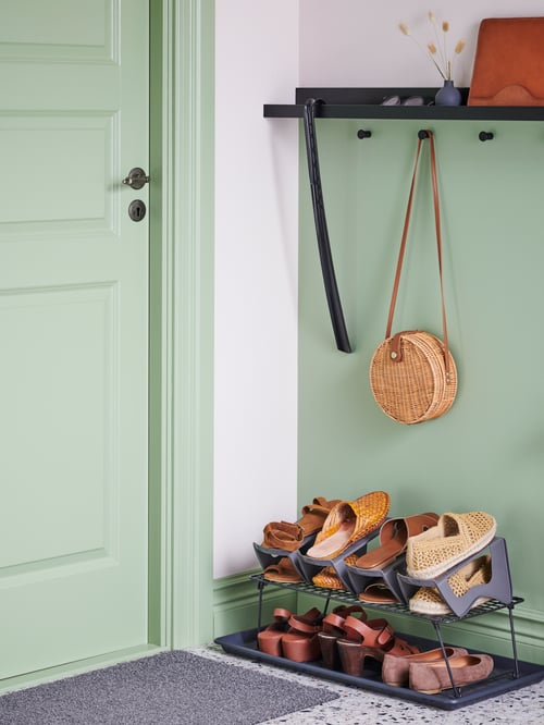 Un rangement à chaussures GREJIG, soigneusement rempli avec l’aide des organisateurs MURVEL, se trouve sur un tapis BAGGMUCK dans un couloir vert clair.
