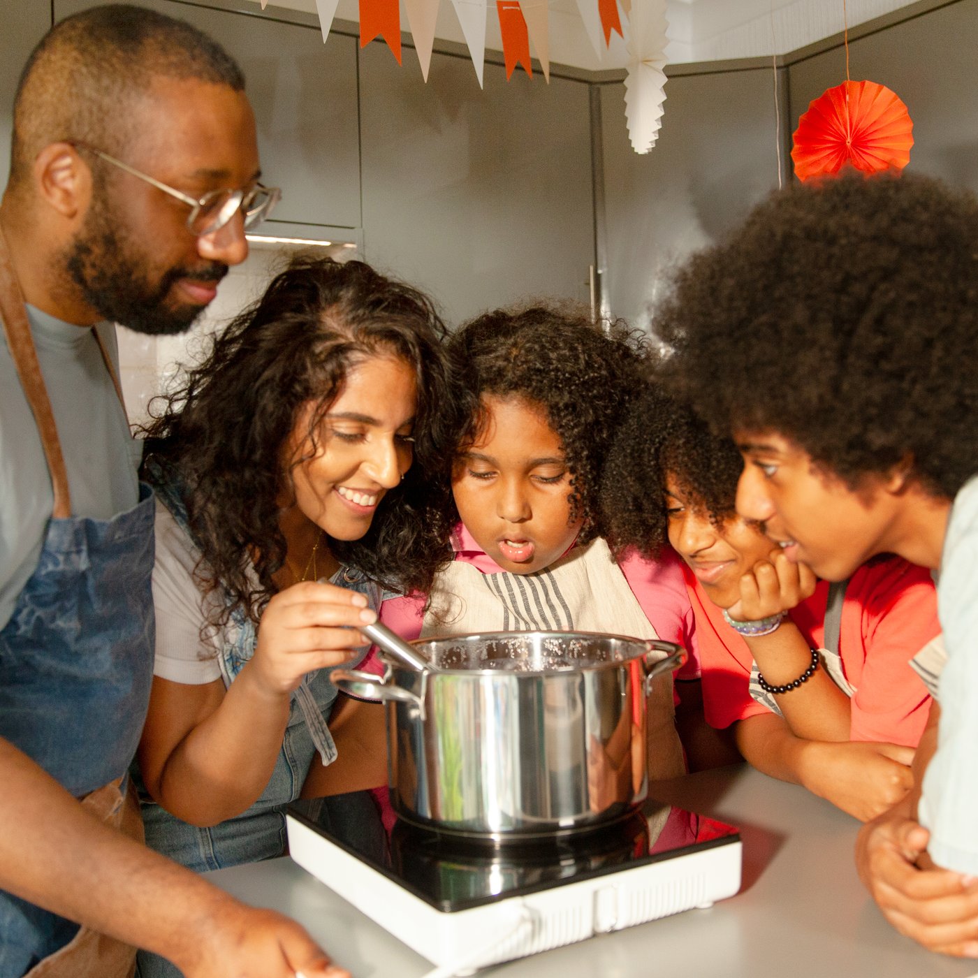 A family of five is stirring an IKEA 365+ pot on a TILLREDA portable induction hob.