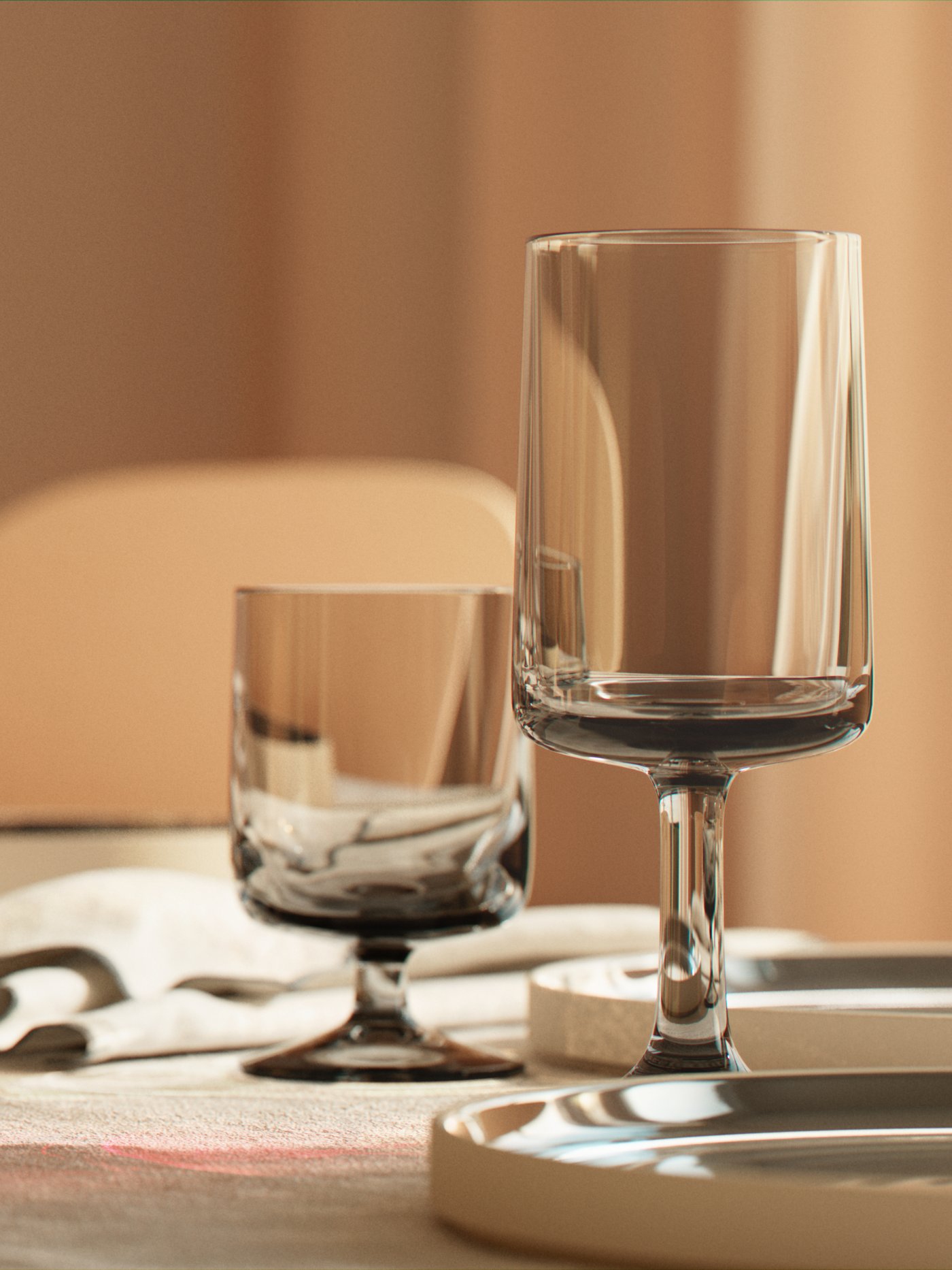 In a dining room, an OMBONAD grey wine glass and goblet are on a table with OMBONAD napkins, plates and linen tablecloth.