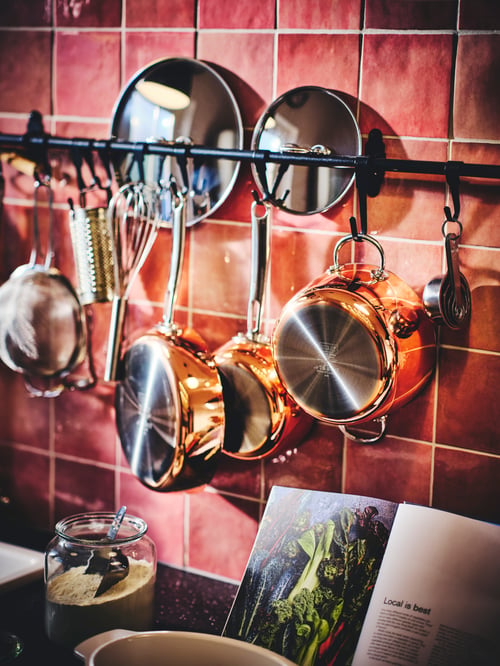 Une cuisine équipée d’un rail mural noir avec plusieurs casseroles et une sauteuse suspendues à des crochets noirs.