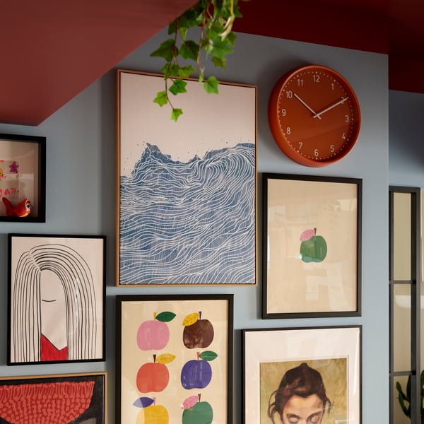 A brightly coloured room with a wall section filled with neatly arranged framed art and an orange BONDIS clock.