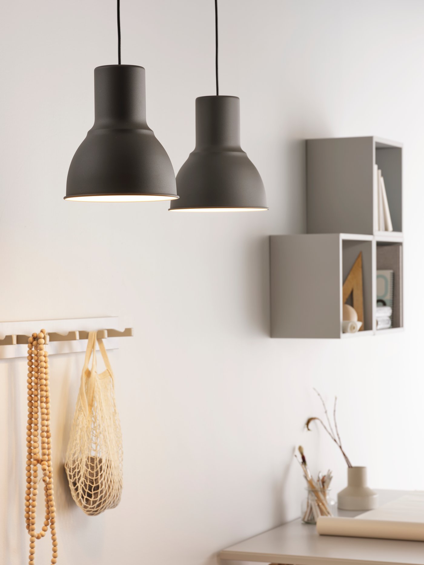 Una pared con un gancho con bolsas colgando y un estante EKET. Por la parte superior se ven dos pantallas de lámparas colgantes encendidas.