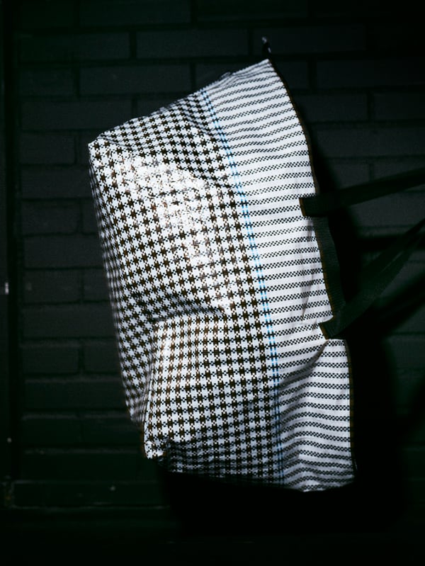 A roomy SAMMANKOPPLA bag with a black and white houndstooth pattern and a shiny texture in a dark room.