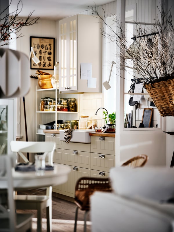 A bright, country-style kitchen and dining area, with beige cabinets, a round table and dried branches in a basket.