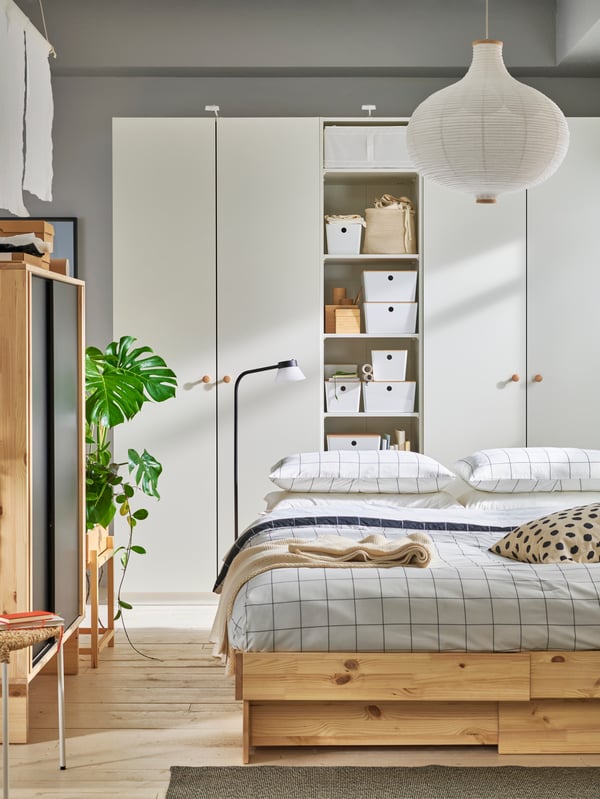 Bedroom in beige and white with bed in natural wood and beige bedding. Combination of white PLATSA wardrobes in back.