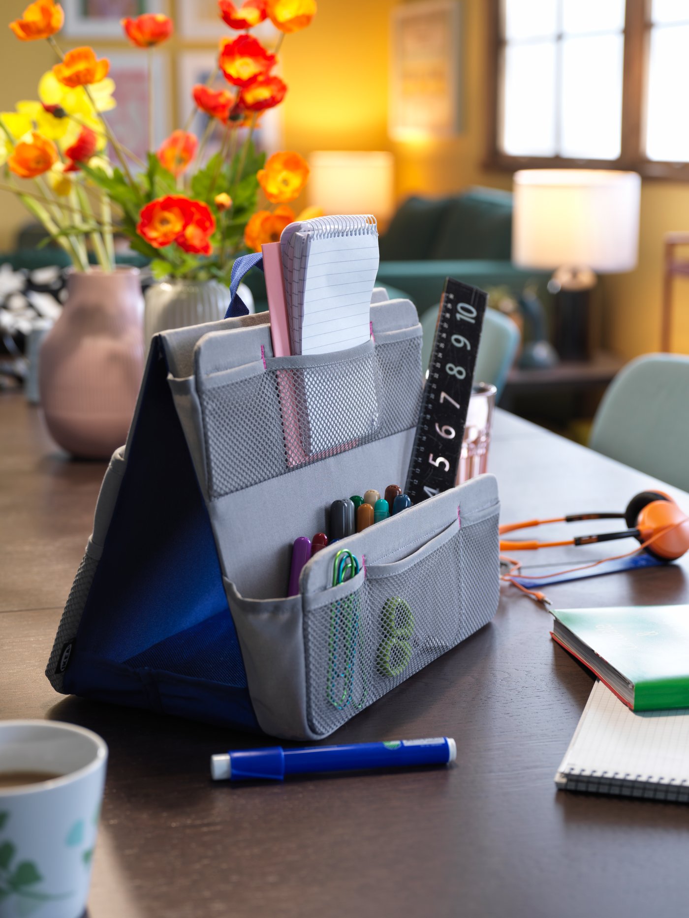 Contenitore per accessori da scrivania ÖVNING su un grande tavolo, tra cuffie, vasi di fiori e una tazzina di caffè.