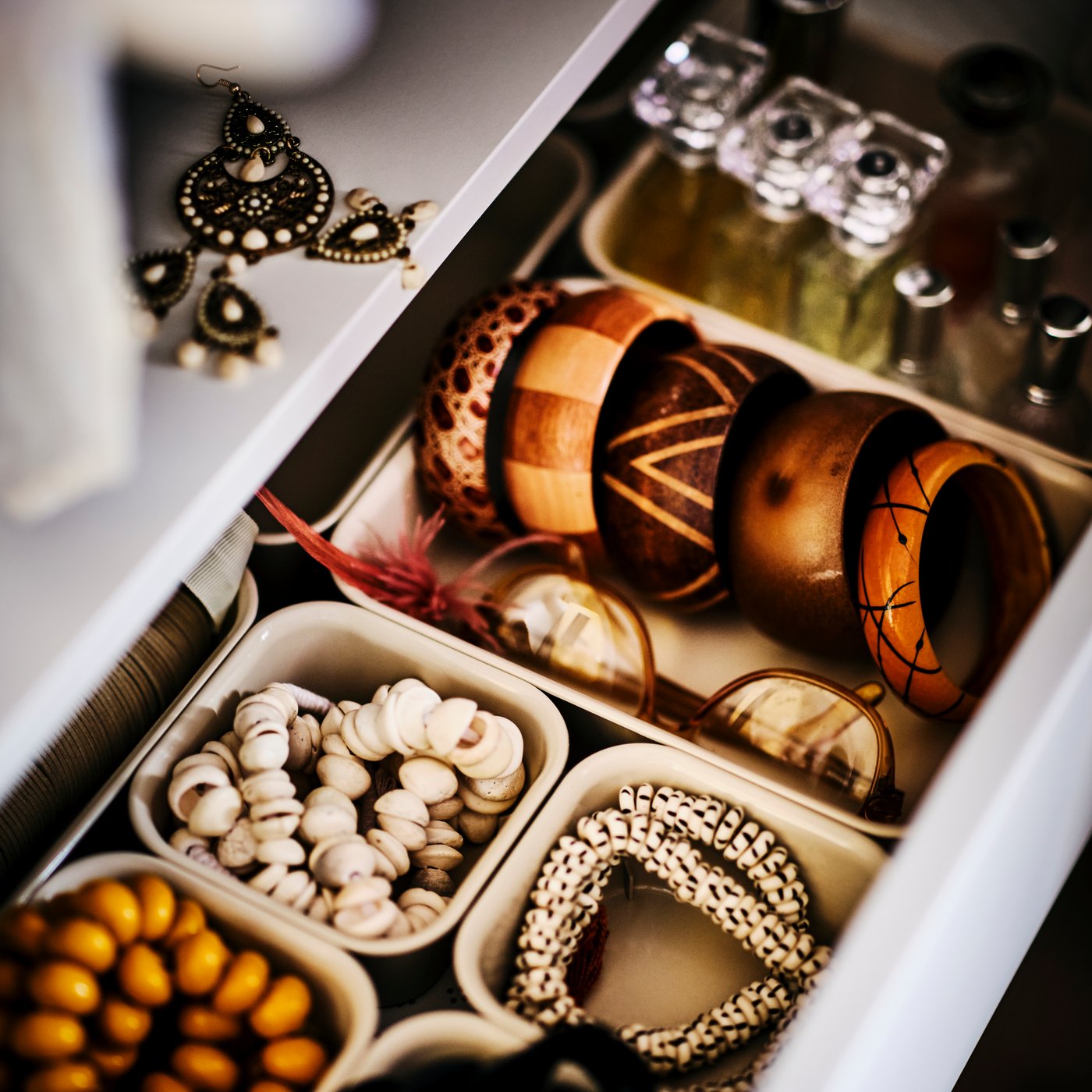 Otwarta szuflada z pojemnikami NOJIG wypełnionymi biżetureria i akcesoriami.