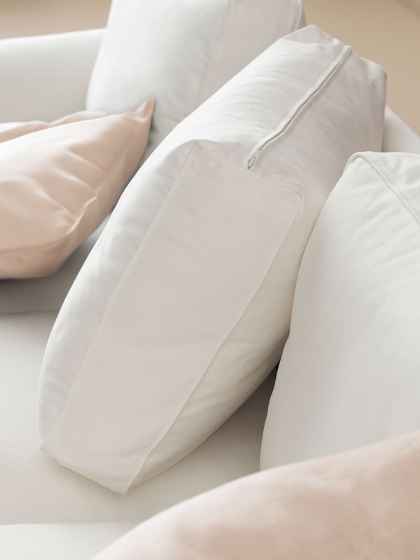The back cushions of an UPPLAND sofa with a white cover, with one cushion sitting at an angle, and some extra cushions.