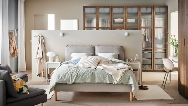 A SAGESUND upholstered bed in a neutral bedroom with BERGPALM bed linen and cushions in off-white and pale blue covers on it.
