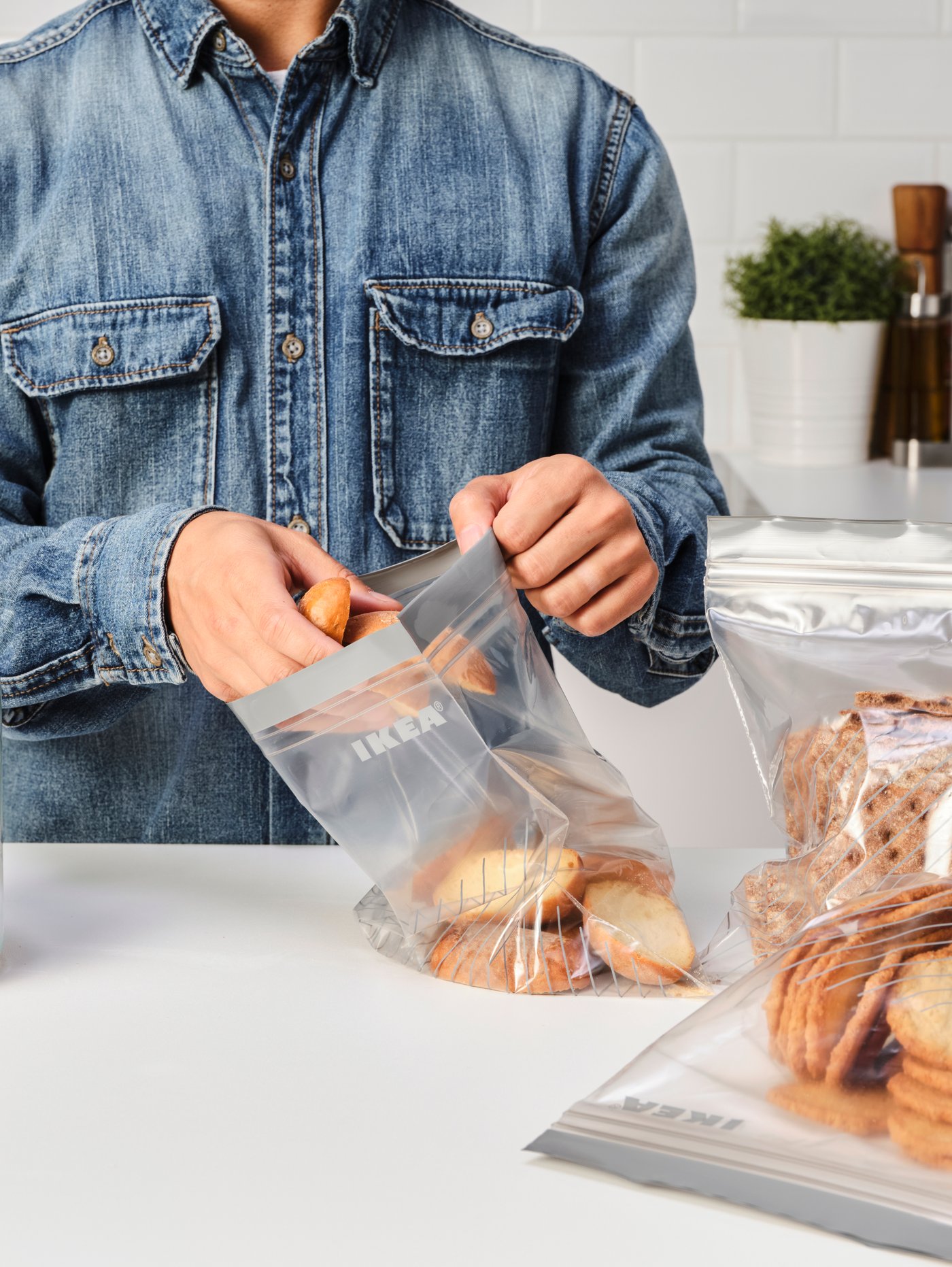 سطح عمل مطبخ أبيض، وثلاثة أكياس من ISTAD يمكن إعادة غلقها بإحكام وشخص يرتدي قميص جينز يضع البقسماط في إحدى الأكياس.