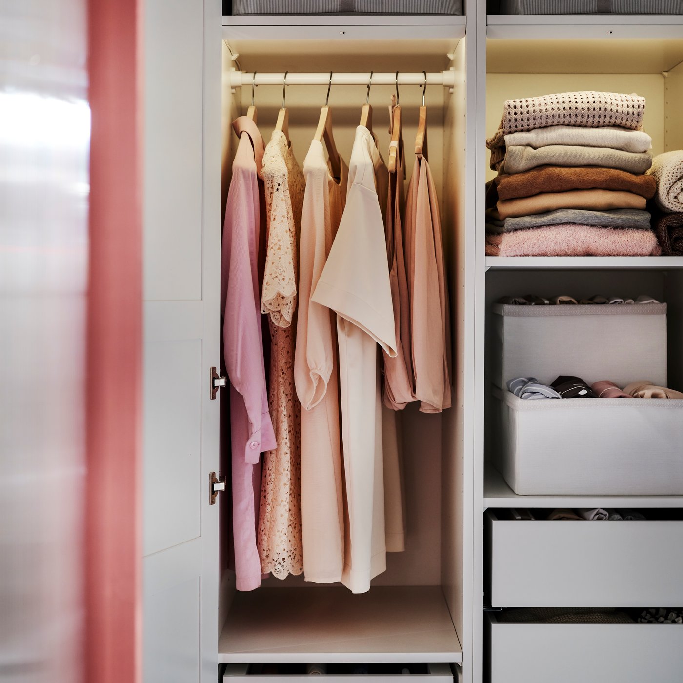 An open PAX wardrobe shows a hanging rail holding clothes on BUMERANG hangers and SKUBB boxes filled with clothes on shelves.