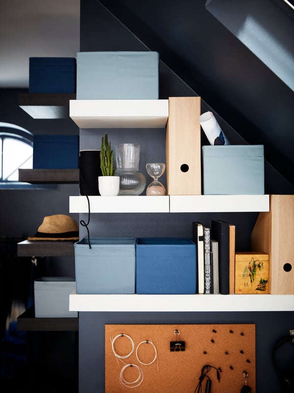 LACK wall shelves of different lengths are mounted to the wall under some stairs. They hold various objects including books.