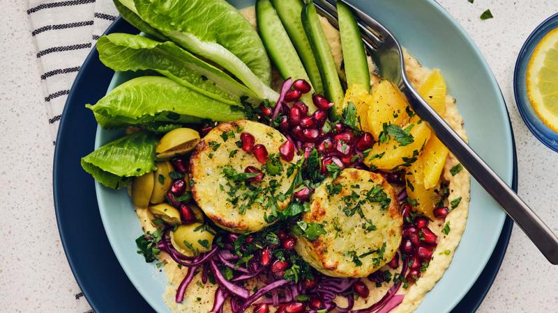 A turquoise plate is placed on top of a blue plate. There is colourful mix of vegetables, fruits, and vegetable medallions.