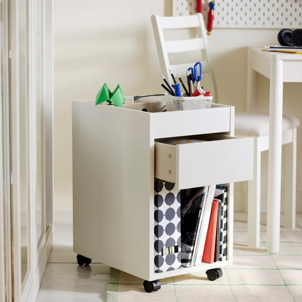 A TONSTAD drawer unit on castors in white with diverse items on and in it, in front of a TONSTAD extendable table and chair.