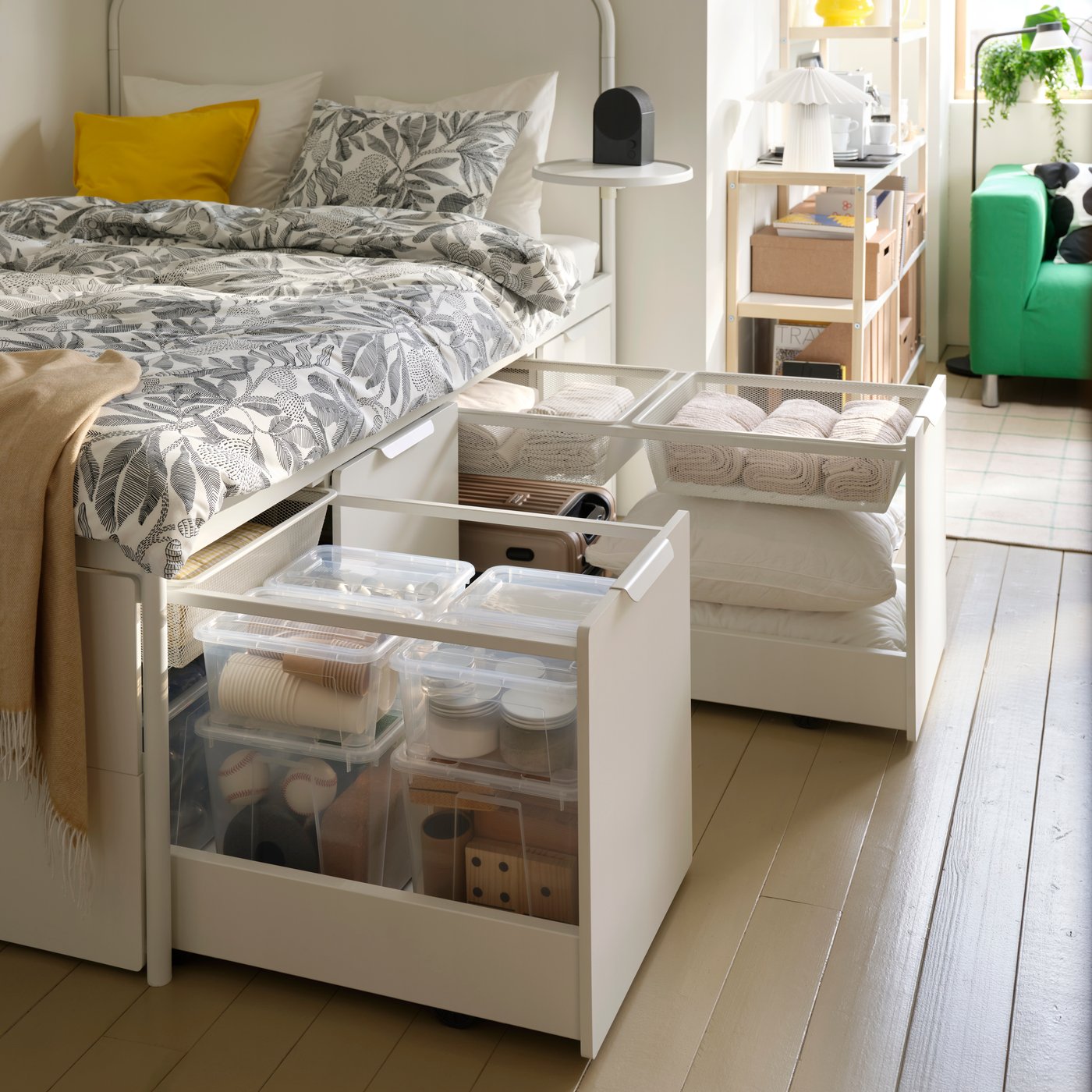 Transparent plastic SAMLA boxes with lids hold sports balls and party supplies in a drawer of a white bed frame with storage.