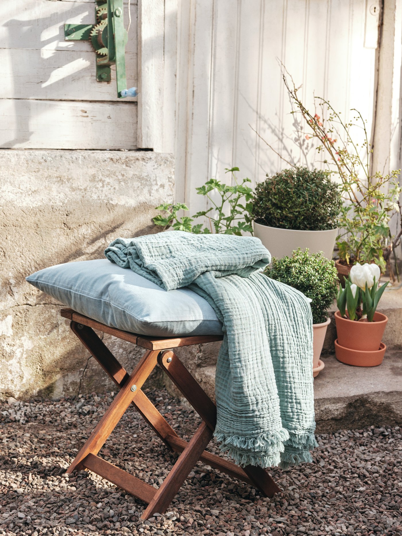 Un patio con piso de piedras con un butaco NÄMMARÖ con un cojín y una manta verdes encima.
