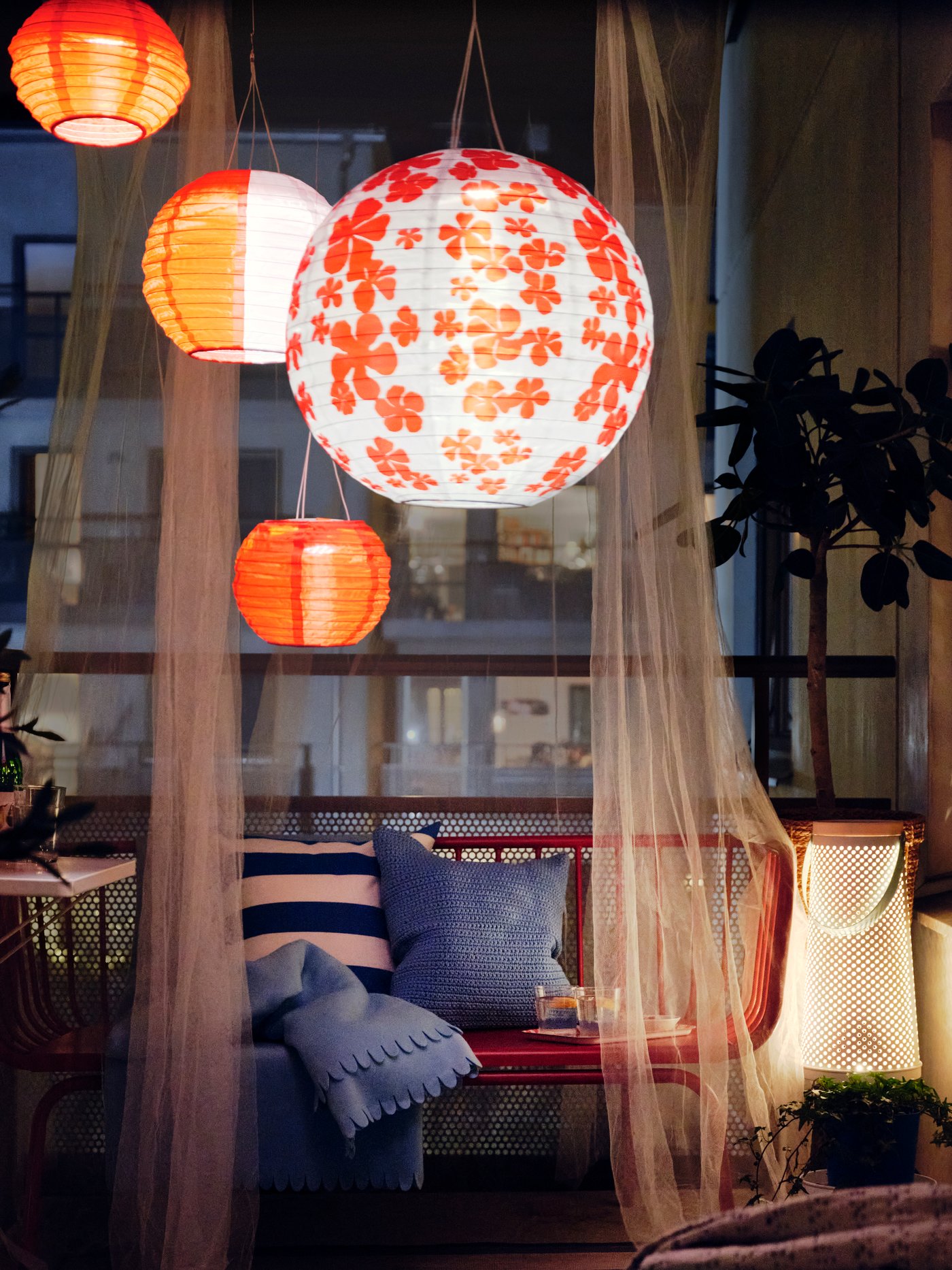 A balcony at night with several SOLVINDEN LED solar-powered outdoor lamps, a BRUSEN outdoor sofa with cushions and a throw.