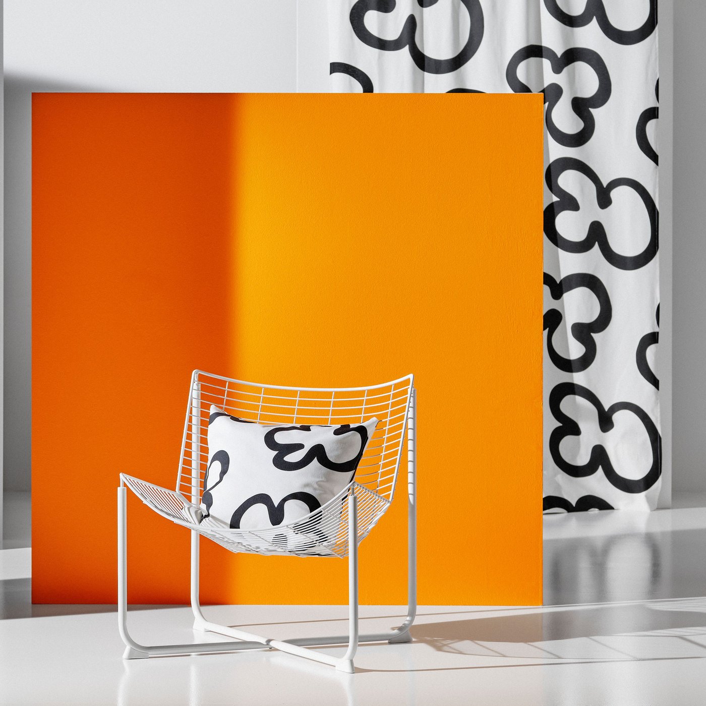 A SKÅLBODA armchair is placed in front of an orange screen. There is a cushion with a KLIPPBRÄCKA cushion cover in the chair.
