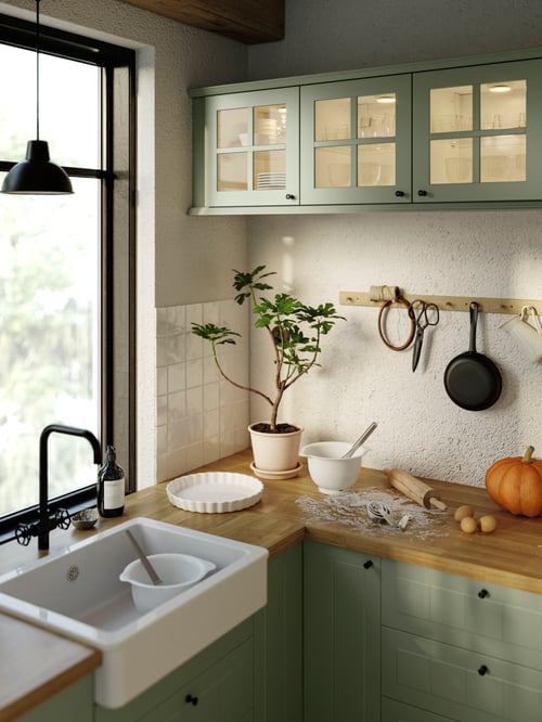 Cottage aesthetic kitchen with ceramic sink bowl with visible front and shiny white glaze, black mixer tap, and wood worktop.