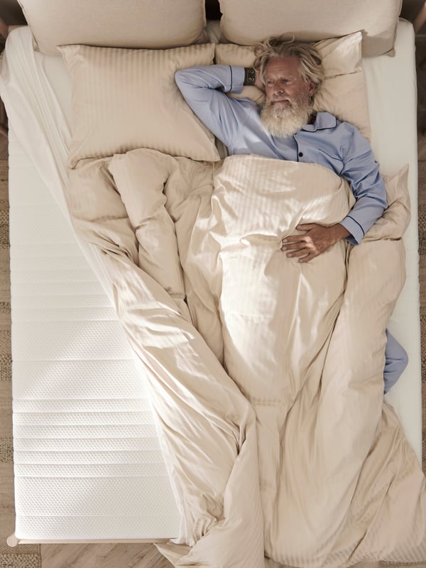 Image en plongée d’un homme dormant sur un matelas ÅNNELAND.
