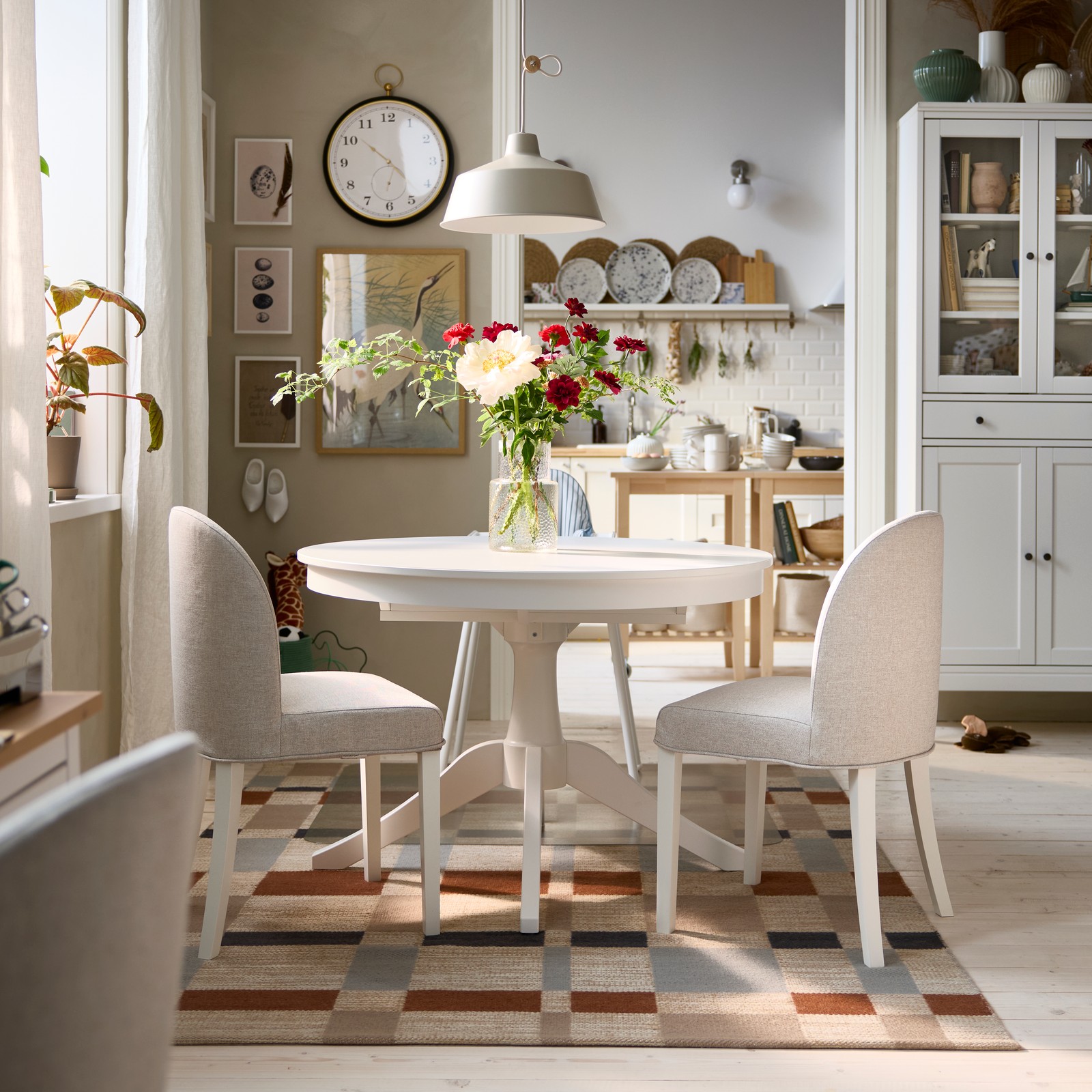 A bright dining area has a white ROSENTORP extendable table, two ROSENTORP chairs and an ANTILOP highchair with tray.