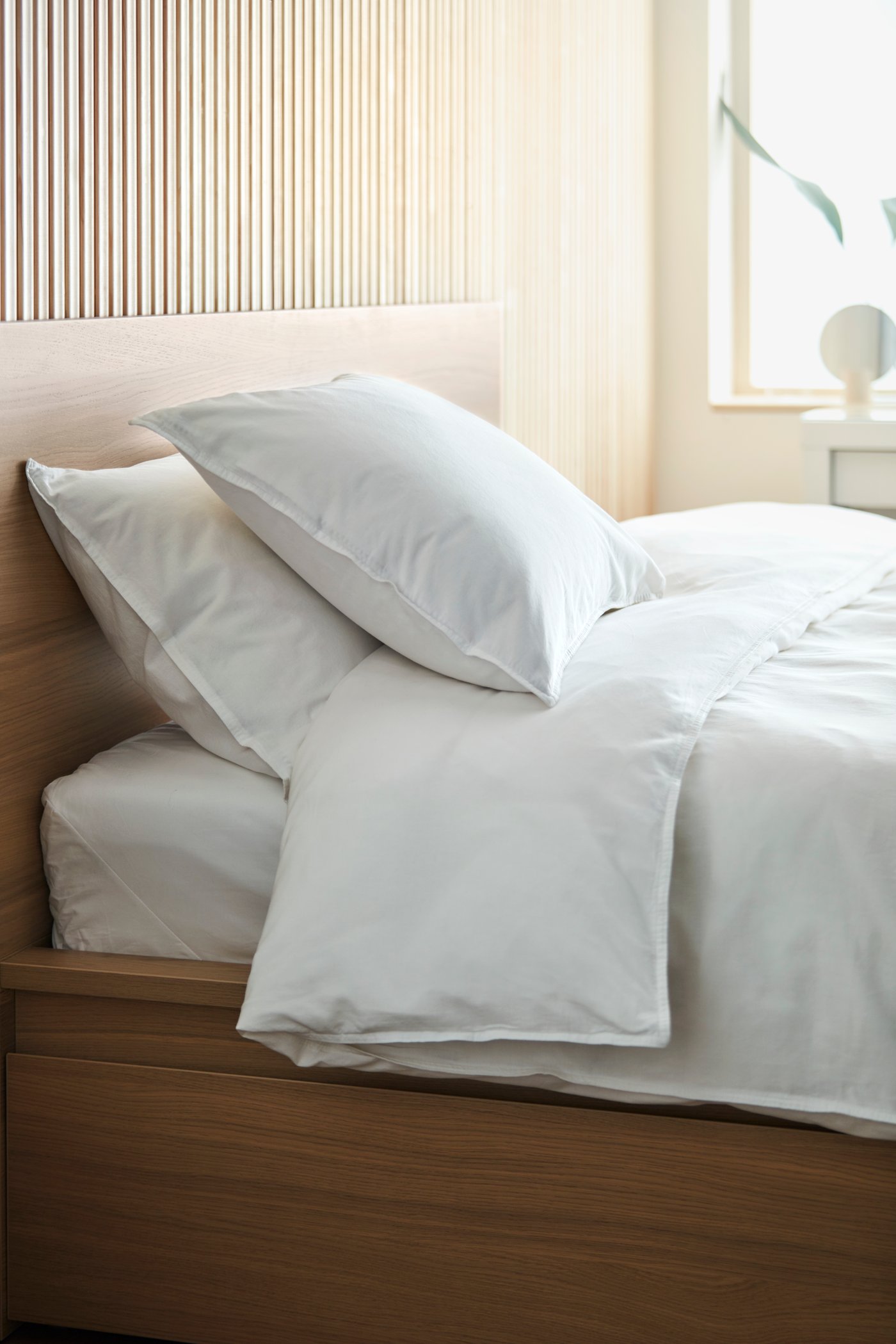 Vitt ÄNGSLILJA påslakansset på en säng med trästomme i ett avskalat, modernt sovrum.