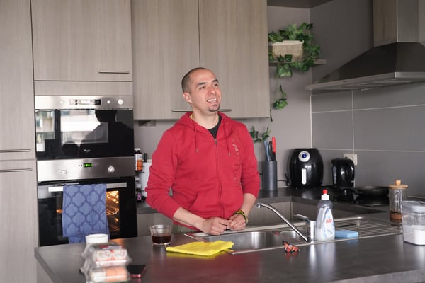Edgar, wearing a red hoodie, stands in his kitchen.