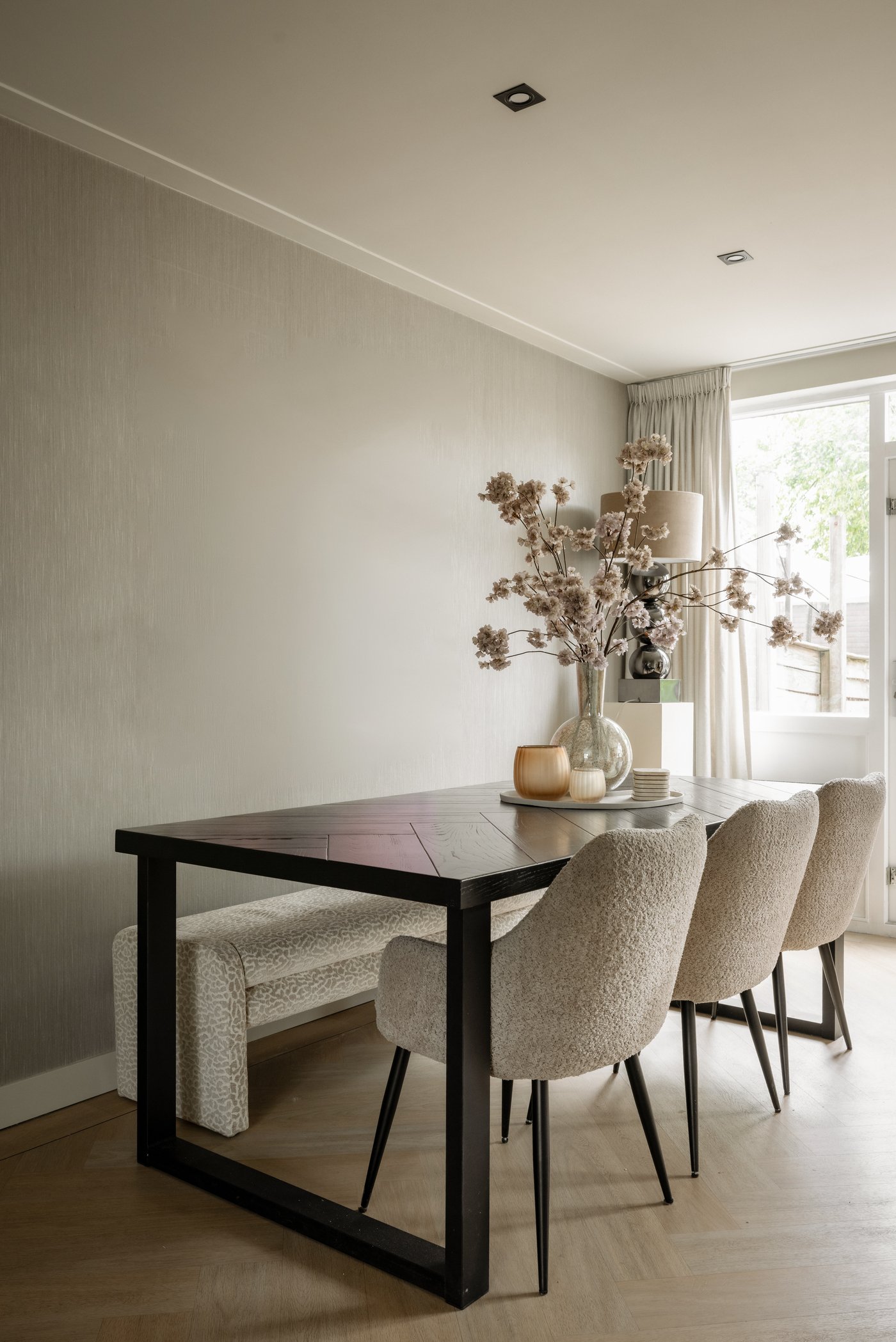 Eethoek in de woonkamer. Aan de ene kant van de langwerpige eettafel staan 3 kuipstoelen, aan de andere kant staat een lange bank.
