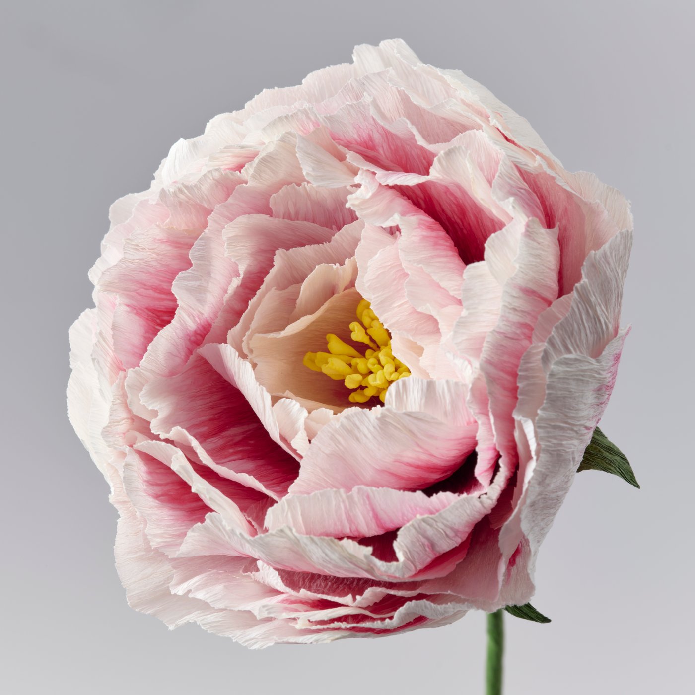 Un dettaglio su un fiore artificiale che ricrea una peonia rosa di carta estremamente realistica